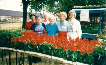 Image of ladies standing in front of a plant staff