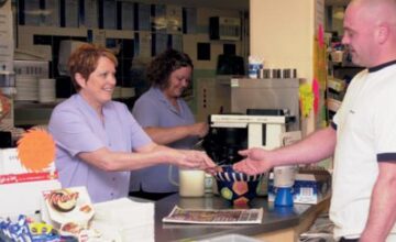 A photo showing a cafe counter and a customer being served