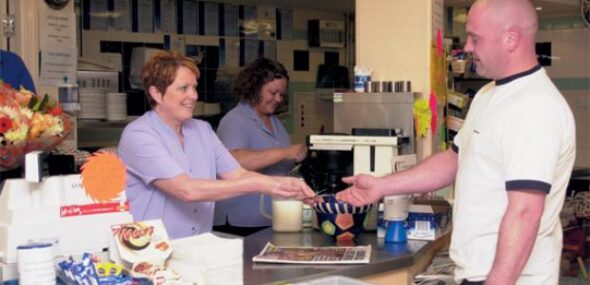 A photo showing a cafe counter and a customer being served