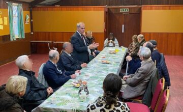 An image of a group of people sitting around a long table listening to a person speaking