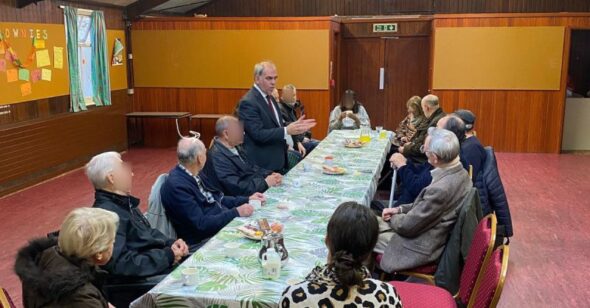 An image of a group of people sitting around a long table listening to a person speaking
