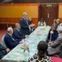 An image of a group of people sitting around a long table listening to a person speaking