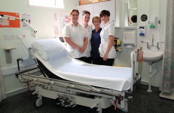 an Image showing 4 people standing beside an examination table