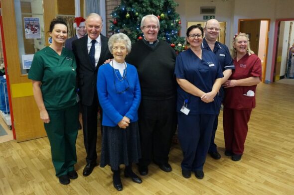 A group of people standing in front of a Christmas tree in a hospital ward