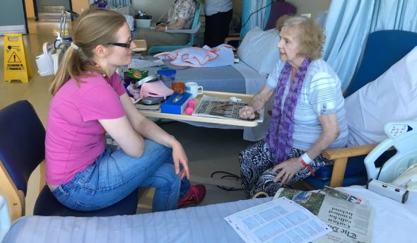A photo of 2 people sitting beside a hospital bed and talking