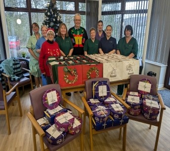 The image shows a group of staff and volunteers in Festive jumpers behind a table laden with Christmas gift bags