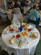 The image shows the beautifully laid table, with bowls of strawberries, plates of sandwiches and scones